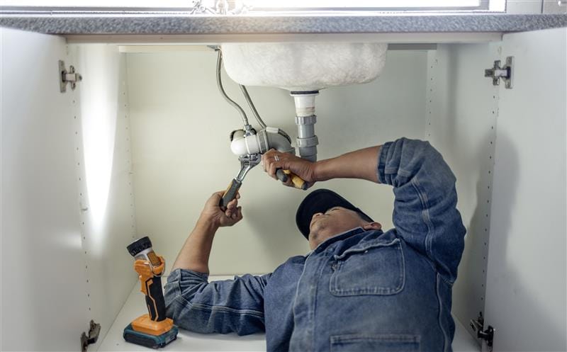 Plumber repairing pipes beneath a bathroom sink in Woodstock